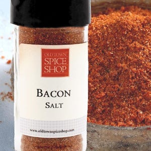May include: A clear glass spice jar with a black lid containing reddish-brown bacon salt. The white label features the red Old Town Spice Shop logo, the text Bacon Salt, and the website address www.oldtownspiceshop.com in black lettering.