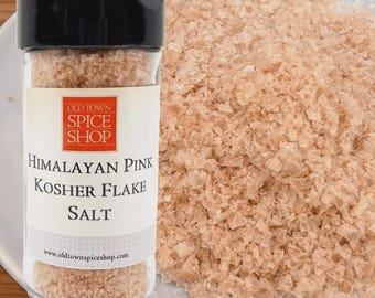 May include: A clear plastic spice jar with a black lid containing Himalayan Pink Kosher Flake Salt. The label features the text Old Town Spice Shop and Himalayan Pink Kosher Flake Salt. A pile of the pink salt flakes sits next to the jar.