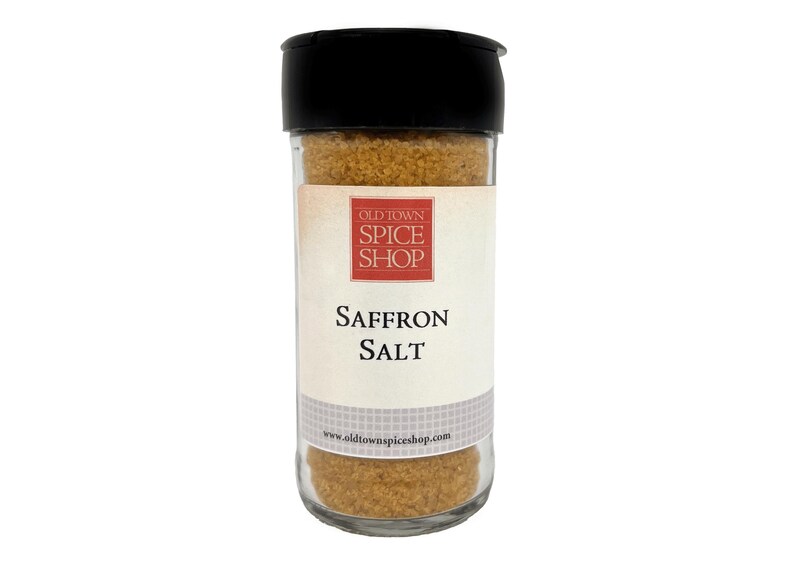 May include: A clear glass spice jar with a black plastic lid containing golden-brown saffron salt. The white label features a red square logo with the text OLD TOWN SPICE SHOP, the words SAFFRON SALT, and the website www.oldtownspiceshop.com.