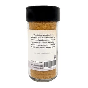 May include: A clear glass spice jar with a black plastic lid, filled with golden-brown saffron sea salt. The label reads: The distinct taste of saffron with pure sea salt crystals creates an uncommonly delicious flavoring! Net wt 3.5 oz (99 g).