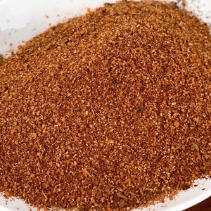 Pu&ograve; includere: Primo piano di un mix di spezie marroni in una ciotola bianca. Il mix di spezie &egrave; composto da piccole particelle finemente macinate.