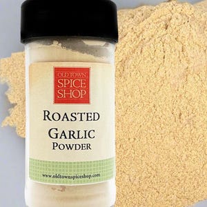 Puede incluir: Un frasco de especias de vidrio transparente con tapa negra que contiene ajo en polvo tostado. La etiqueta presenta un cuadrado rojo con el texto OLD TOWN SPICE SHOP, seguido de las palabras ROASTED GARLIC POWDER y el sitio www.oldtownspiceshop.com.