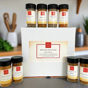 May include: A white gift box labeled "Around The Globe Gift Box" with spice jars. The jars have black lids and white labels with red accents. Spices include Chimichurri Blend, Berry, Thai Red Curry, and Pure 101.