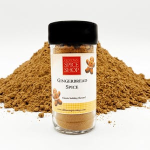 May include: A clear glass jar of Gingerbread Spice with a black lid, set against a backdrop of ground spice. The label reads "Old Town Spice Shop" and "Gingerbread Spice". The jar features gingerbread man illustrations and the text "Classic holiday flavors!"
