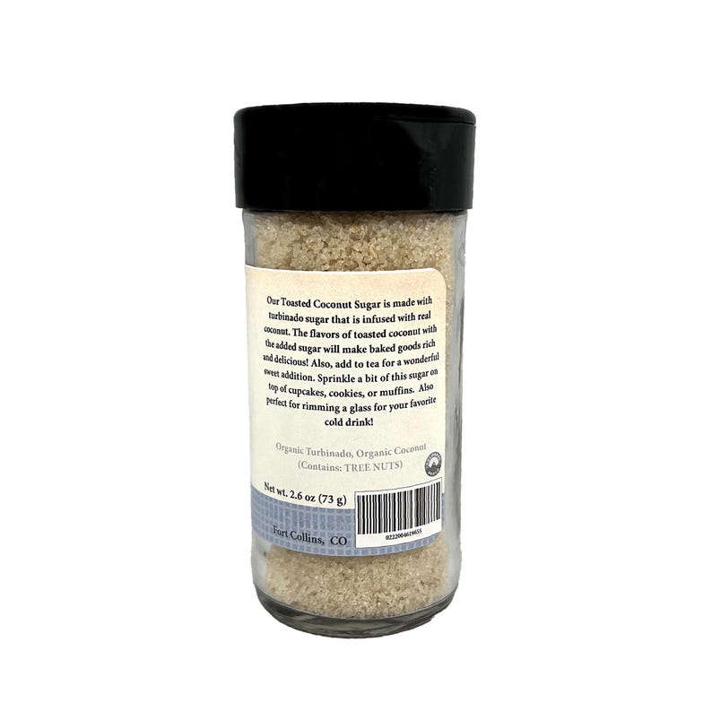 May include: A clear glass jar with a black lid containing light brown sugar. The label states "Our Toasted Coconut Sugar" and details ingredients and uses. Net weight is 73 grams.
