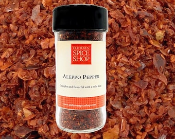 May include: A glass jar of Aleppo pepper with a black lid. The label reads "Old Town Spice Shop" and "Aleppo Pepper" with the description "Complex and flavorful with a mild heat". The jar is filled with red pepper flakes.