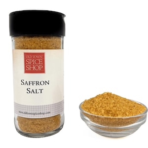 May include: A clear glass spice jar with a black lid containing golden-yellow saffron salt. The label features the text Old Town Spice Shop and Saffron Salt. Next to the jar is a small clear glass bowl filled with the same golden-yellow saffron salt.