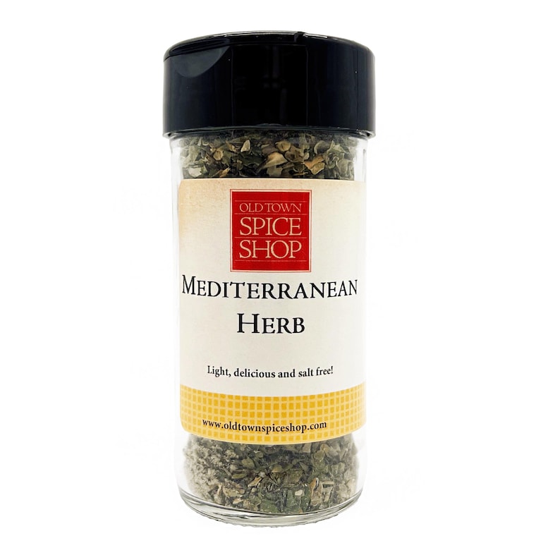 May include: A clear plastic spice jar with a black lid containing dried green herbs. The label features the text Old Town Spice Shop, Mediterranean Herb, and Light, delicious and salt free!, along with the website www.oldtownspiceshop.com.