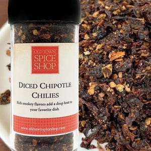 May include: A clear glass spice jar with a black lid containing diced chipotle chilies. The label reads Old Town Spice Shop, Diced Chipotle Chilies, Rich smokey flavors add a deep heat to your favorite dish, and www.oldtownspiceshop.com.