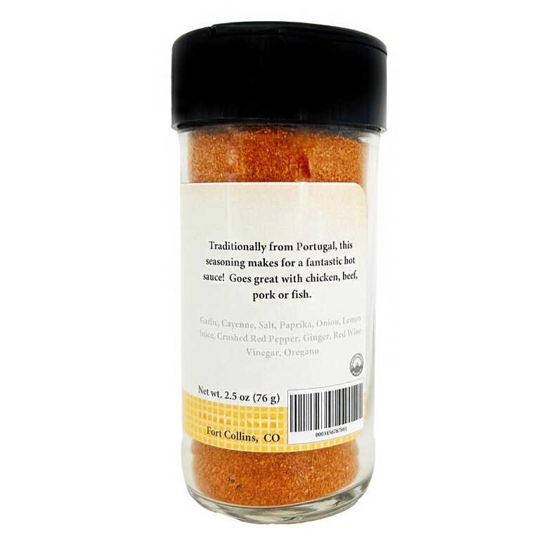 May include: A clear glass spice jar with a black lid, filled with a reddish-orange seasoning blend. The label reads "Traditionally from Portugal" and lists ingredients. Net weight is 2.5 oz (76 g).