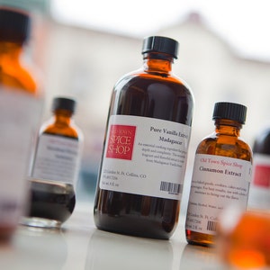 May include: Four glass bottles of vanilla and cinnamon extract. The bottles are brown glass with white labels. The largest bottle is labeled "Pure Vanilla Extract Madagascar" and is from "Old Town Spice Shop". The smaller bottle is labeled "Cinnamon Extract" and is also from "Old Town Spice Shop".