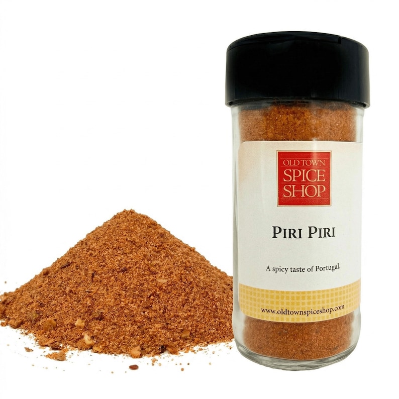 May include: A clear glass jar of Piri Piri spice from Old Town Spice Shop with a black lid. A pile of the reddish-brown spice is next to the jar. The label says "A spicy taste of Portugal."