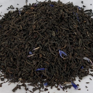 May include: A close-up of a pile of loose leaf black tea with blue cornflower petals.