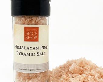 May include: A clear glass spice jar with a black lid containing Himalayan pink pyramid salt. The label features the text Old Town Spice Shop, Himalayan Pink Pyramid Salt, and the website address www.oldtownspiceshop.com. A pile of salt sits beside.