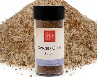 Könnte beinhalten: Ein klares Glas mit schwarzem Deckel, beschriftet mit "Spiced Chai Sugar" von Old Town Spice Shop, steht vor einem Haufen Zuckerkristallen. Das Etikett hat ein rot-weißes Logo. Die Website www.oldtownspiceshop.com ist aufgedruckt.