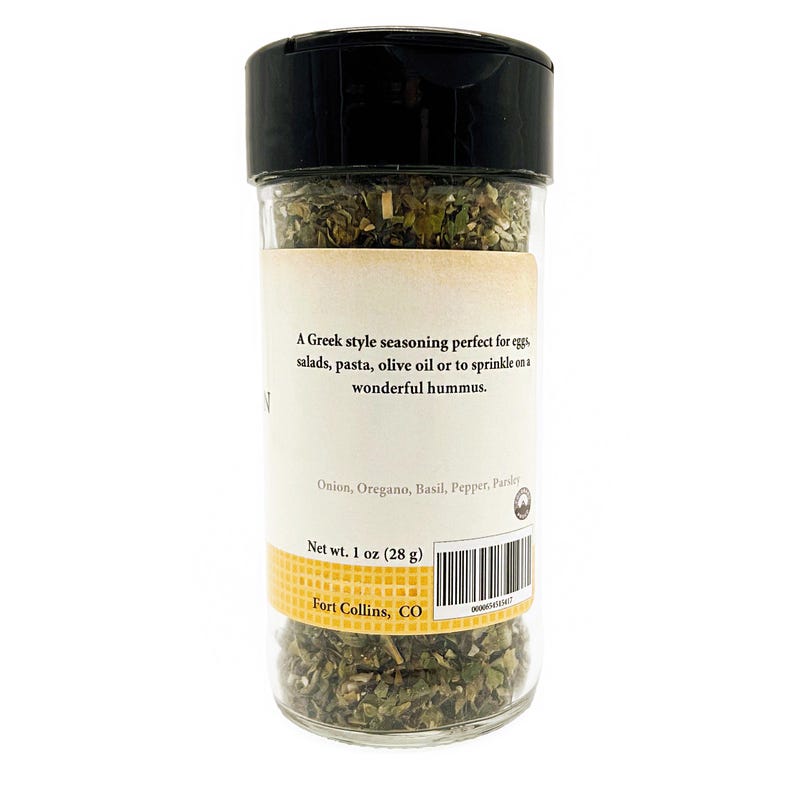 May include: A clear plastic spice jar with a black lid containing dried green herbs. The label reads: A Greek style seasoning perfect for eggs, salads, pasta, olive oil or to sprinkle on a wonderful hummus. Onion, Oregano, Basil, Pepper, Parsley. Net wt. 1 oz (28 g). Fort Collins, CO.