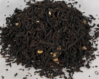 May include: A close-up of a pile of loose leaf black tea with pieces of dried fruit. The tea is a dark brown color and the fruit is a light brown color.
