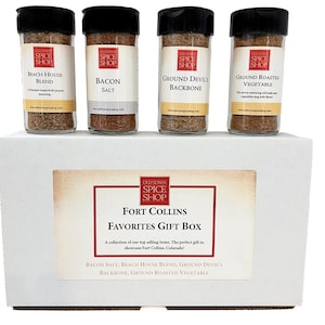 A white "Fort Collins Favorites" gift box open to reveal four glass jars of gourmet spices including Bacon Salt and Devil's Backbone.