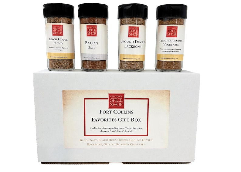 A white "Fort Collins Favorites" gift box open to reveal four glass jars of gourmet spices including Bacon Salt and Devil's Backbone.