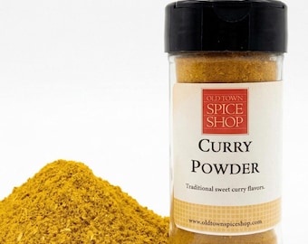May include: A clear plastic spice jar with a black lid containing yellow curry powder. The label reads Old Town Spice Shop, Curry Powder, Traditional sweet curry flavors, and www.oldtownspiceshop.com. A pile of yellow curry powder sits beside the jar.