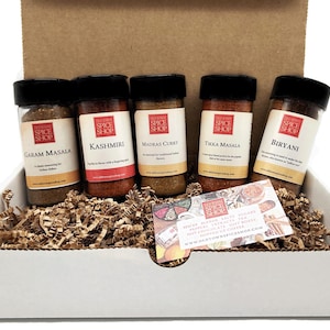 May include: A gift box containing five spice jars with black lids and labels. The labels read "Garam Masala", "Kashmiri", "Madras Curry", "Tikka Masala", and "Biryani". The box is filled with brown packing material and a small card.