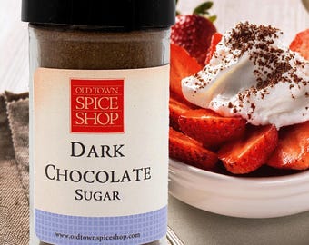 Könnte beinhalten: Ein durchsichtiges Gewürzglas aus Glas mit schwarzem Deckel, gefüllt mit dunkelbraunem Schokoladenzucker. Das Etikett zeigt ein rotes Quadrat mit dem Text OLD TOWN SPICE SHOP und darunter DARK CHOCOLATE SUGAR sowie die Website www.oldtownspiceshop.com.