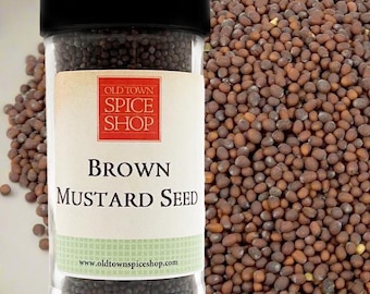 May include: A clear glass spice jar with a black lid filled with small, round, dark brown mustard seeds. The label features a red square with the text OLD TOWN SPICE SHOP and the words BROWN MUSTARD SEED in black, with the website address below.
