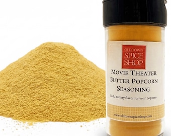 Puede incluir: Un frasco de plástico transparente con tapa negra que contiene condimento amarillo Movie Theater Butter Popcorn Seasoning de Old Town Spice Shop, junto a un pequeño montón del fino polvo amarillo.