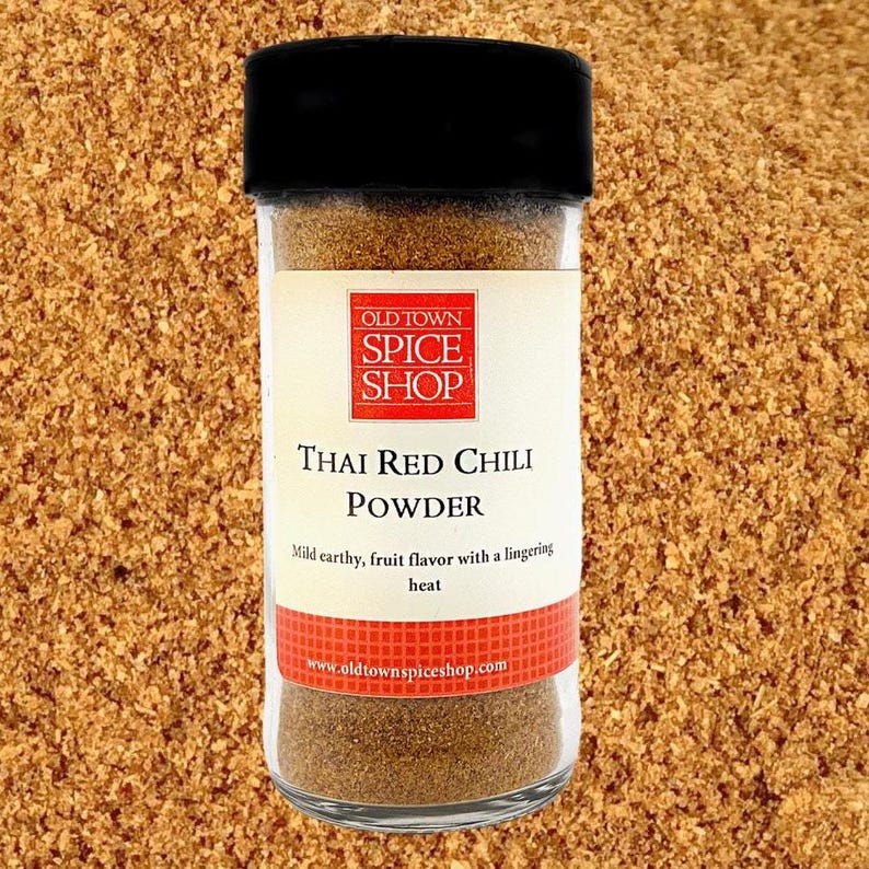 Jar of Thai Red Chile powder in front of the ground Thai pepper