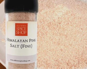 May include: A clear glass spice jar with a black lid containing fine Himalayan pink salt. The label features a red square logo with the text Old Town Spice Shop, followed by the words Himalayan Pink Salt (Fine) and a website URL.