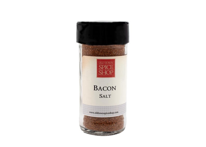 Puede incluir: Un frasco de vidrio con tapa negra lleno de sal de tocino marr&oacute;n. La etiqueta dice "Old Town Spice Shop" en rojo y "Bacon Salt" en negro.