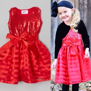 May include: Red sequined dress with a red satin bow and red and white striped tulle skirt. The dress is sleeveless and has a scoop neckline.