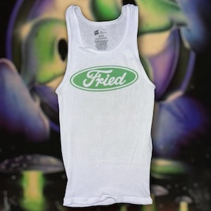 May include: White ribbed vest top featuring the word "Fried" in green, within a green oval. A classic style vest top, suitable for casual wear. The background is a blurred, colourful design.