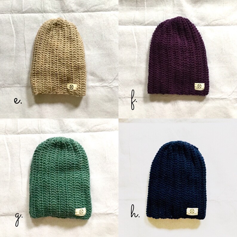 May include: Four crocheted beanies in different colors: beige, purple, green, and navy blue. Each beanie has a small, white label with a symbol on it.