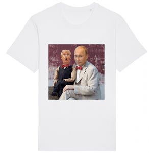 Puede incluir: Camiseta blanca con un estampado gráfico de dos hombres, uno sentado y el otro de pie sobre su regazo. El hombre sentado lleva un traje blanco con una pajarita roja. El hombre de pie lleva un chaleco a rayas blanco y negro con una pajarita roja.