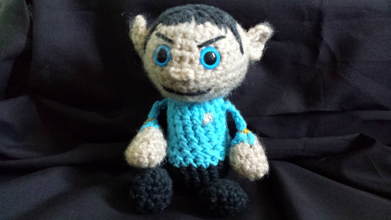 May include: A crocheted plush toy of a character with pointed ears, black hair, and a blue uniform. The toy has blue eyes and a serious expression.