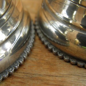 May include: Close-up of two silver-colored, ornate objects with a reflective, polished surface. The objects have a ridged design and a scalloped edge. The background is a light brown wooden surface.