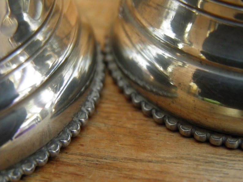 May include: Close-up of two silver-colored, ornate objects with a reflective, polished surface. The objects have a ridged design and a scalloped edge. The background is a light brown wooden surface.