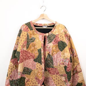 Pode incluir: Um casaco acolchoado com um design de patchwork de vários tecidos florais e texturizados em tons de amarelo mostarda, rosa seco, verde azeitona e creme. O casaco tem um decote redondo, mangas compridas e um fecho de um único botão.