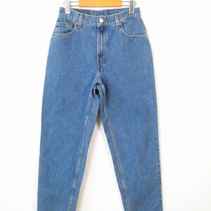Może przedstawiać: Dżinsy z jasnoniebieskiego denimu wiszące na drewnianym wieszaku. Dżinsy mają wysoki stan i prosty kr&oacute;j nogawek.
