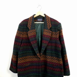 May include: A vintage patterned blazer in a mix of colours including green, brown, red, and blue. The blazer features a geometric design, a notched collar, two front pockets, and a single-button closure. The lining is green.