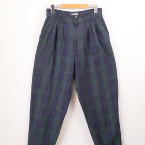 May include: High-waisted trousers featuring a dark green and navy blue plaid pattern. These trousers include a front button closure, a zip fly, and pleated detailing at the waistband. The design incorporates side pockets and a tapered leg silhouette.