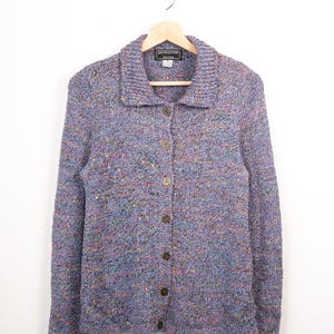 Può includere: Un cardigan a maniche lunghe con chiusura a bottoni in maglia multicolore con tonalità di blu, viola e macchie di giallo e arancione. Il capo presenta un colletto e una chiusura frontale con bottoni con un'etichetta del marchio South Cotton.