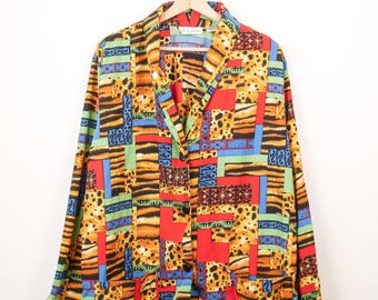 May include: A long-sleeve button-down shirt featuring a vibrant patchwork design with tiger stripes, leopard spots, and solid blocks of red, blue, and green. The garment includes a notched collar and two large patch pockets on the front lower section.