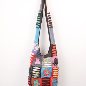 Peut inclure: Un sac besace composé de divers empiècements en tissu aux couleurs noir, rouge, bleu, orange et rose. Le sac présente des appliqués décoratifs tels que des fleurs, un signe de paix et des détails à fentes horizontales, avec une longue bandoulière.