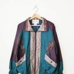 May include: A vintage teal, purple, and tan zip-up jacket with a patterned collar and shoulder accents. The jacket has a high collar, two front pockets, and elastic cuffs. The brand name "Westport Ltd" is visible on the collar.