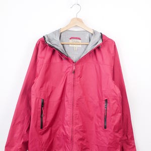 May include: A bright pink hooded jacket with a full-length front zipper, long sleeves, and two vertical zippered pockets on the front. The interior is lined with light gray fabric and features a Cabela's brand label at the inner neckline.