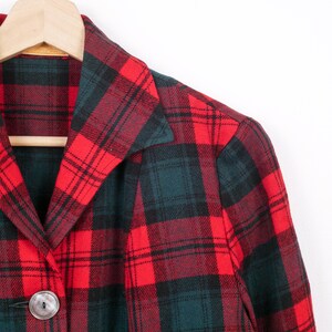May include: A red and green plaid jacket with a large silver button. The jacket is hanging on a wooden hanger. The plaid pattern is a classic design, with a mix of red, green, and black lines.