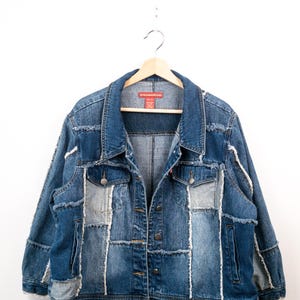 May include: A blue denim jacket featuring a patchwork design with frayed edges, a classic collar, long sleeves, and a front button closure. The garment includes two chest pockets with button flaps and a red interior label reading Americana Studio.