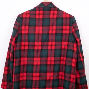 May include: A red, black, and green plaid blazer hanging on a silver hanger. The back of the blazer is visible, showcasing the classic pattern. The fabric appears to be a medium weight, suitable for cooler weather.